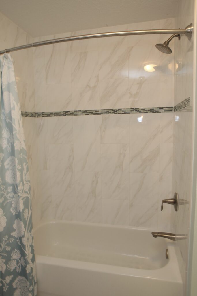 Tub and shower with white marble-look tile surround, mosaic accent band and curved shower rod in a Tampa hall bath