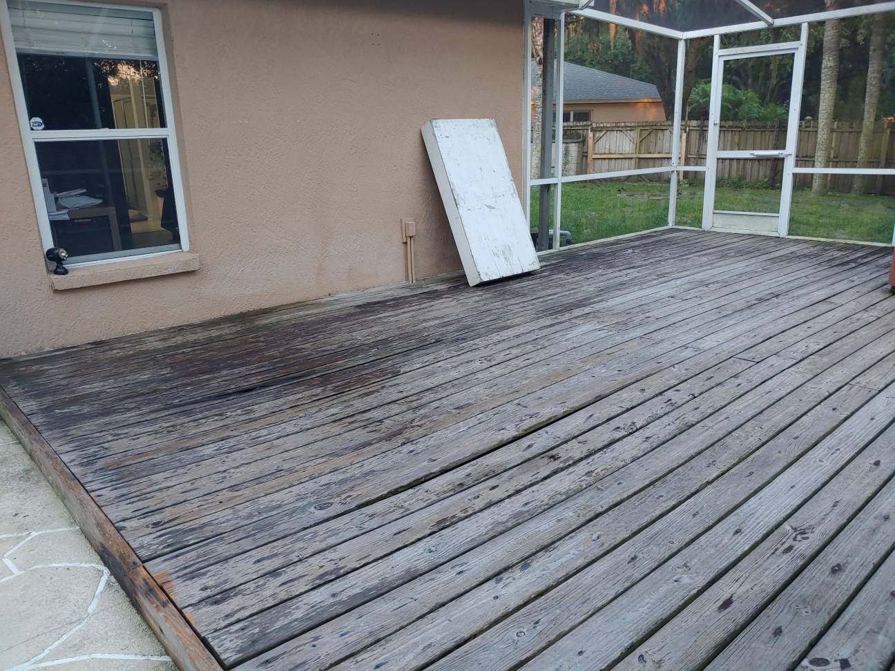 Weathered gray wood deck boards inside a screened Florida lanai showing wear and discoloration