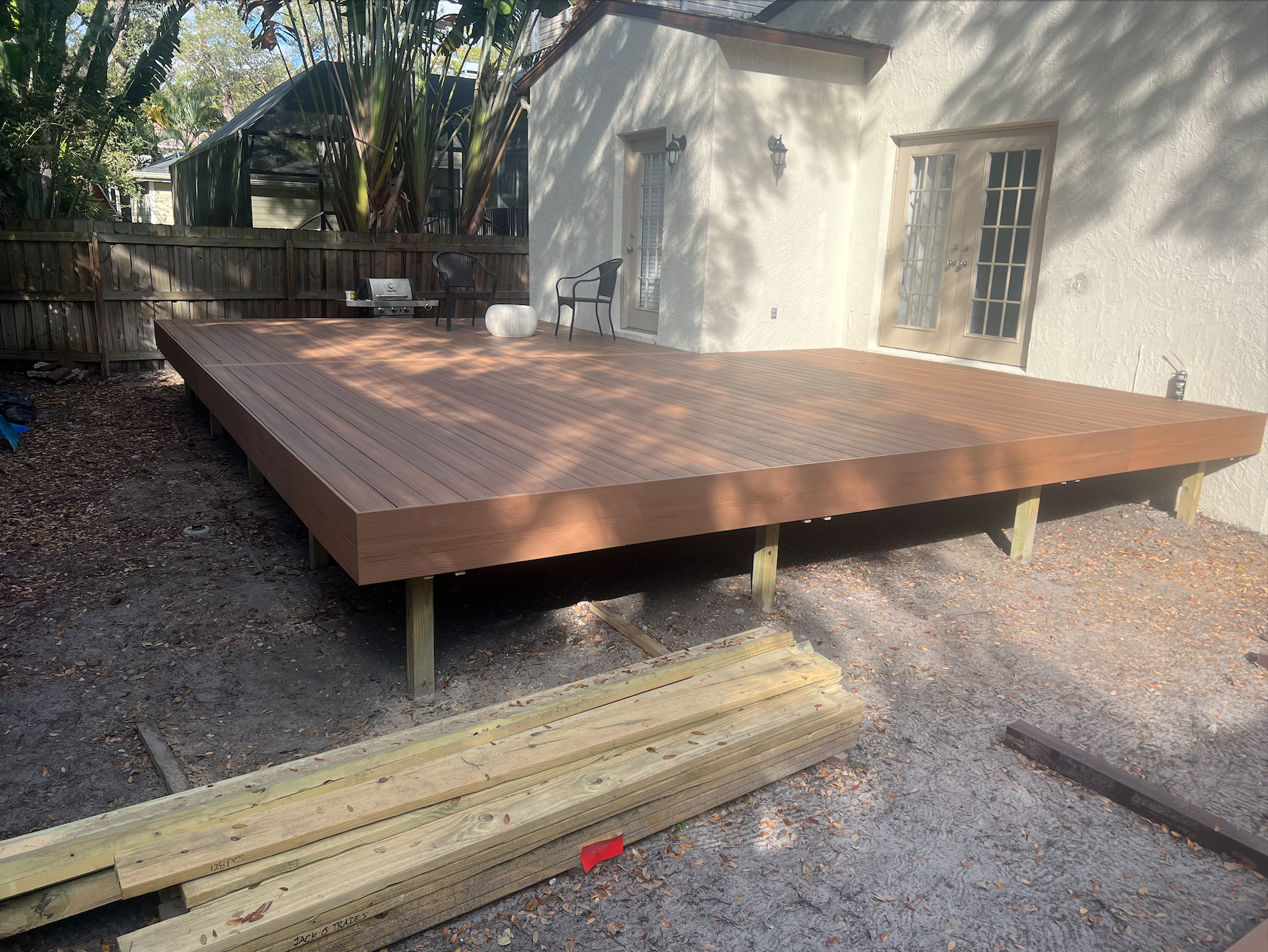New pressure-treated deck frame and decking going in beside a stucco house on a gravel base